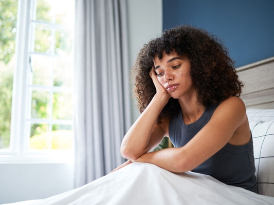 thoughtful woman sitting on bed natural light