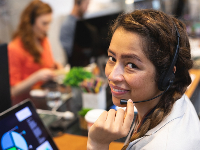 Woman wearing a headset in an office setting with blurred colleagues in the background